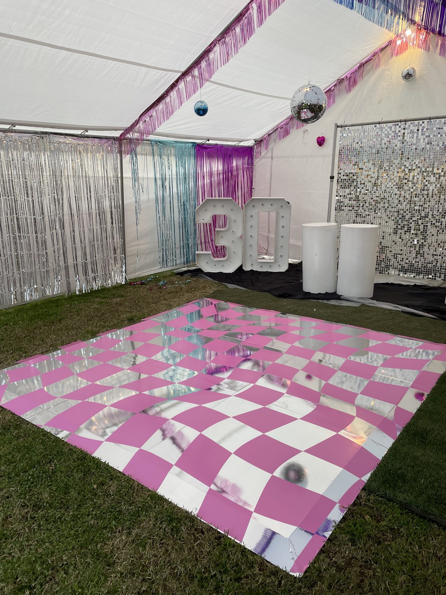 Pink checkerboard transfer decal applied over a silver metallic vinyl dance floor in an event tent